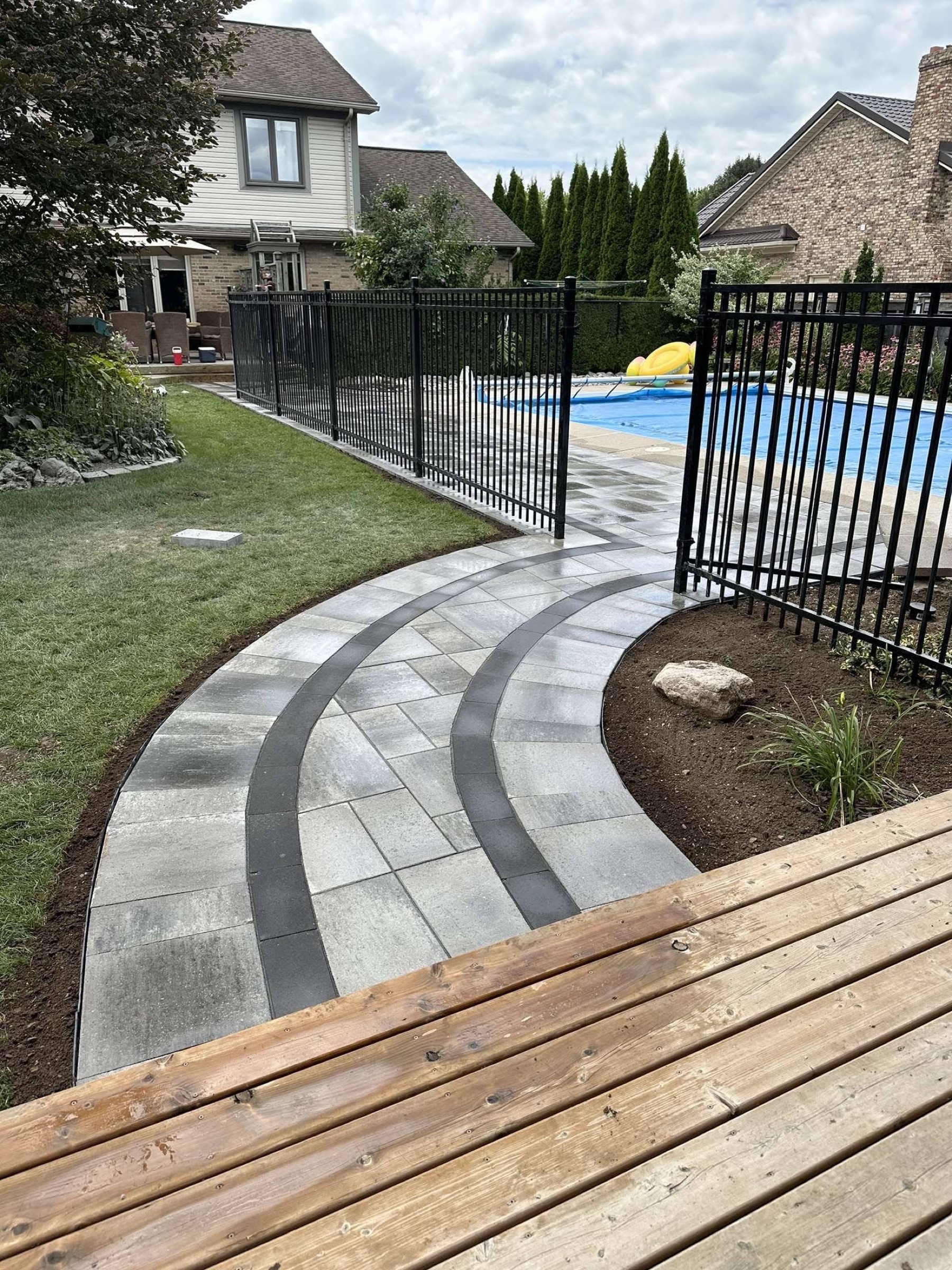 Curved walkway with dark banding beside a pool fence